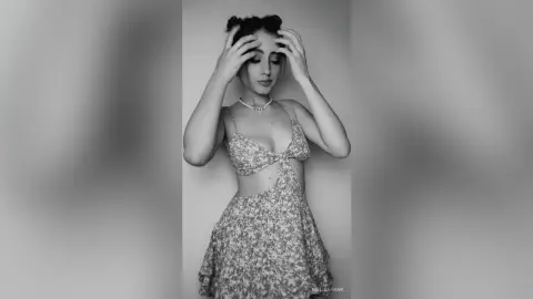 Elegant woman in a floral sundress and pearl necklace posing against a minimalist background in black and white.