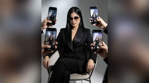 Stylish woman in a black blazer and sunglasses surrounded by smartphones reflecting her portrait in a studio.