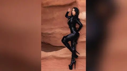 Stylish woman in a sleek black bodysuit and high boots posing against a desert rock formation.