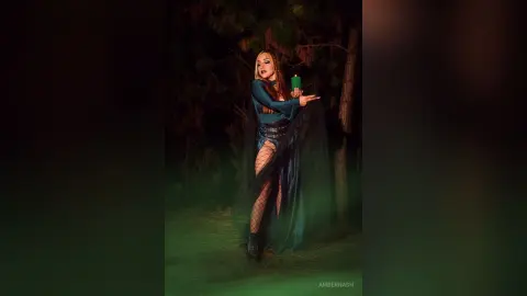 AmberNash — Mystical woman in a dark flowing gown holding a glowing green candle in a moody, dark forest setting.