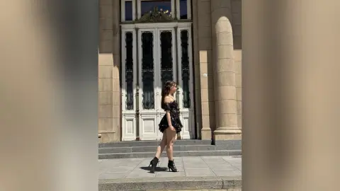 Elegant woman in a black cocktail dress standing before a grand classical building entrance.