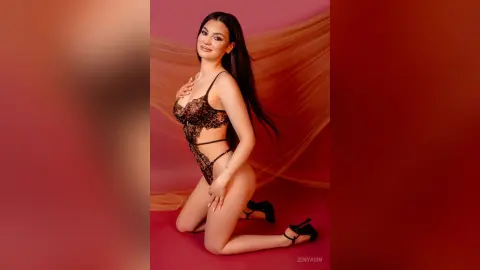 Elegant woman in black lace lingerie posing against a warm red draped background in a romantic mood.