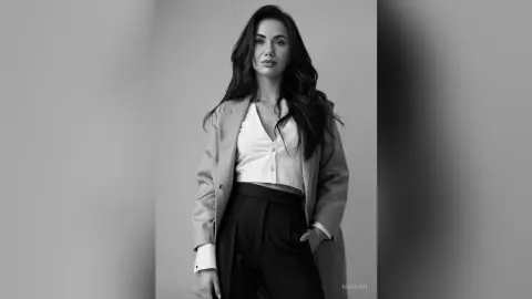 Elegant woman in a white blouse and blazer posing for a sophisticated black and white studio portrait.