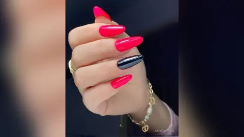Close-up of a hand with long pink and black almond-shaped manicured nails wearing gold jewelry.