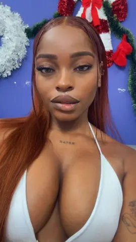 Beautiful woman with long red hair in a white halter top posing against a festive blue and red holiday background.