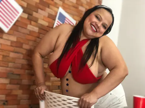 Smiling woman in a red halter top posing against a brick wall in a bright indoor setting.