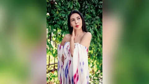 Elegant woman in a white floral off-the-shoulder dress posing in a lush green garden setting.