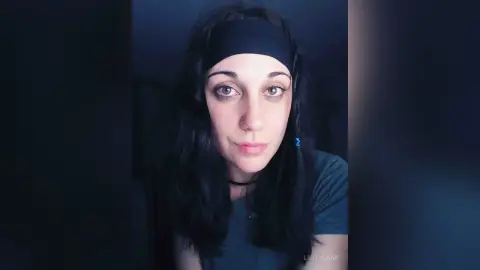Young woman with dark hair and black headband in a moody, dimly lit indoor setting.