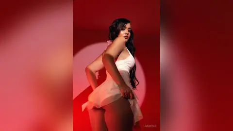 LaraCole poses in a white babydoll slip against a red background, looking back over her shoulder to show her bare buttocks.