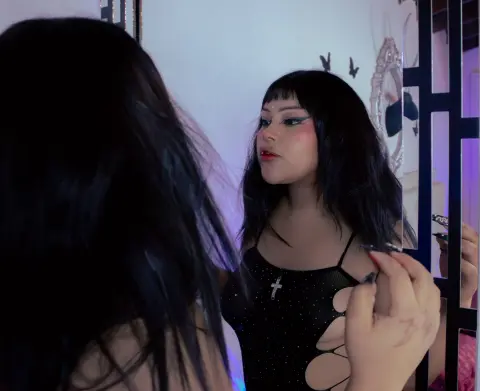 Young woman with dark hair and winged eyeliner in a black cutout top looking into a mirror with a moody vibe.