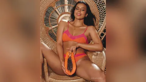 Smiling woman in orange bikini relaxing in a wicker chair for a tropical summer mood.