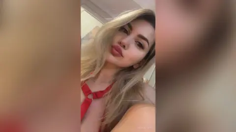 RaisaAllens poses close-up wearing a red halter top that shows off her cleavage and blonde hair.