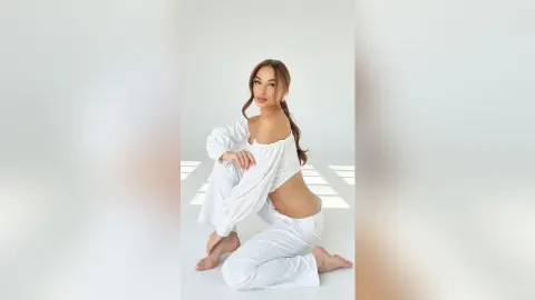 Beautiful woman in white loungewear sitting in a bright, minimalist studio with a serene mood.