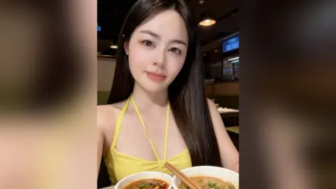 Smiling young woman in a yellow halter top enjoying a meal at a dimly lit restaurant.