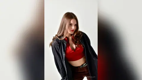 Young woman in a red crop top and black jacket posing against a white background with a confident mood.