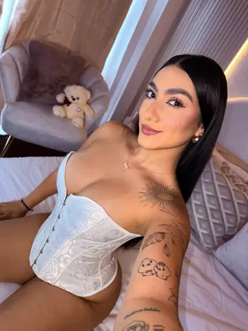Young woman in a white lace corset sitting on a bed with a cozy, soft aesthetic.