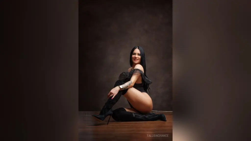 Glamorous woman in red lace lingerie and gold heels posing against a dark studio background.
