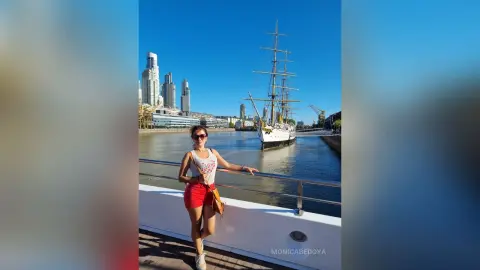 Woman in white tank top and red shorts smiling on a sunny boat tour by the Puerto Madero skyline.