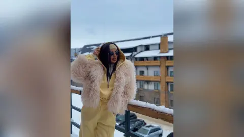 Woman in a cozy cream faux fur jacket and yellow tracksuit relaxing on a snowy balcony.