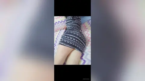 Woman in a black and white patterned mini dress relaxing on a colorful zigzag patterned bedspread.