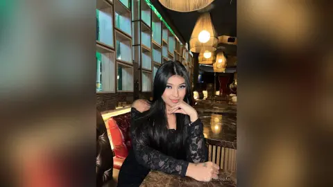 Elegant woman in a black lace dress sitting at a luxury bar with warm ambient lighting.