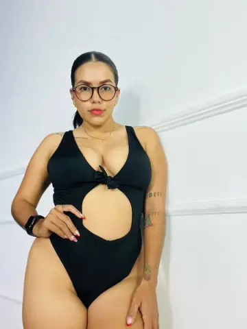 Curvy woman in a black cutout one-piece swimsuit posing against a white wall in a minimalist setting.