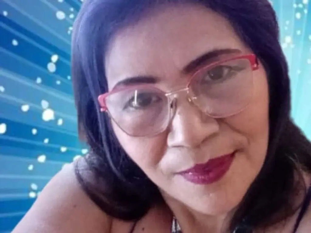 Smiling woman with dark hair and pink glasses posing against a blue starburst background.