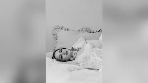 Elegant woman in white lace lingerie relaxing on a bed in a dreamy black and white portrait.