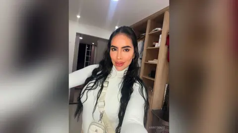 Smiling woman in a white long-sleeve turtleneck posing in a modern walk-in closet.