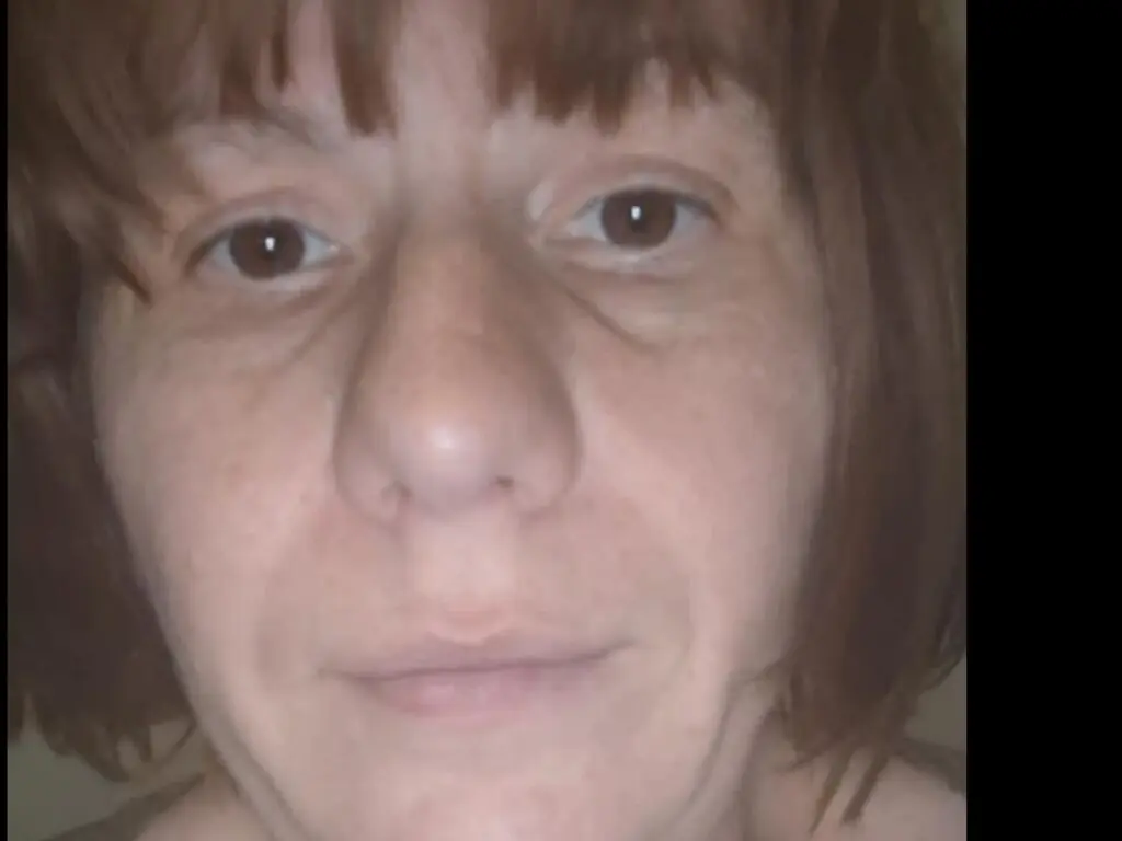 Close-up portrait of a woman with brown hair and a neutral expression in soft indoor lighting.