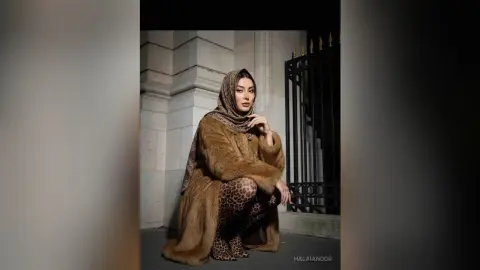 Elegant woman in a brown fur coat and patterned hijab posing against a classic stone building background.
