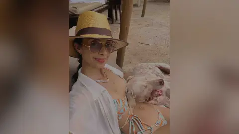 LucyMartin wears a straw hat and sunglasses while relaxing outdoors in a white shirt and patterned bikini top.