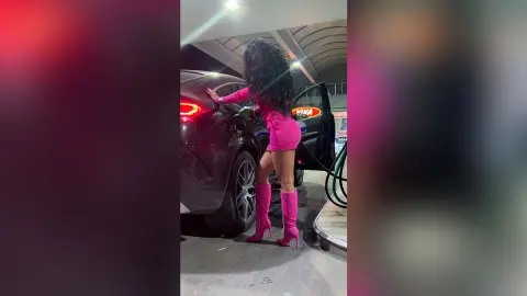 NicoleBella stands next to a black car wearing a tight pink mini dress and matching pink high-heeled boots.