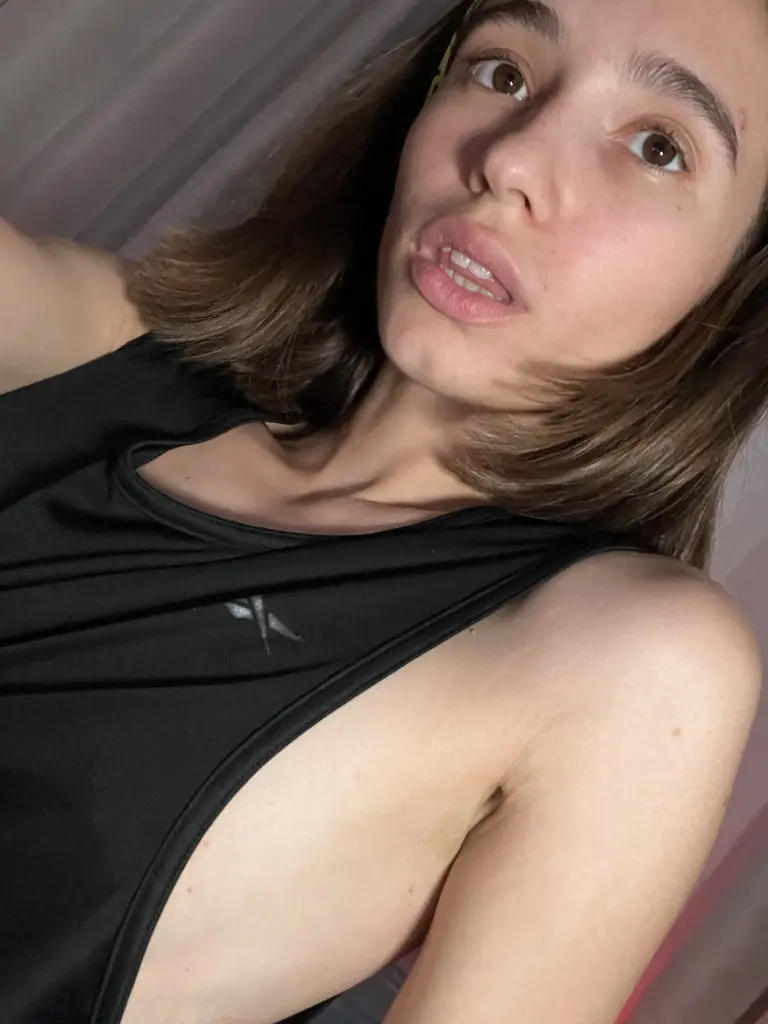 MariaRomanovich looks into the camera with long brown hair, wearing white headphones and showing her bare shoulders and chest.