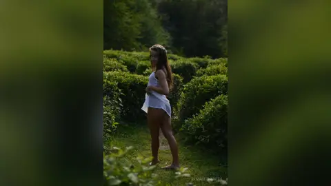 Young woman in a white summer dress standing in a lush green garden during a dreamy golden hour sunset.