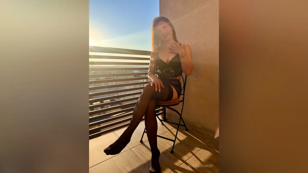 AlessiaHarp — AlessiaHarp sits on a balcony chair wearing black lace lingerie and sheer black stockings during sunset.