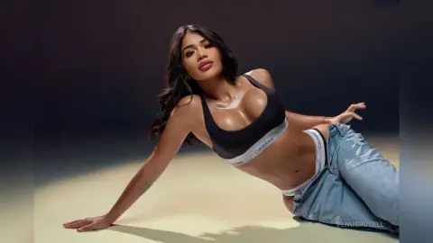 Beautiful woman in black Calvin Klein sports bra and denim jeans posing confidently in a studio setting.