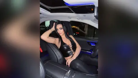 Stylish woman in a black lace bodysuit relaxing in the leather seat of a luxury car with ambient lighting.