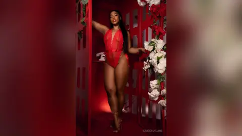 Glamorous woman in a red lace bodysuit posing in a romantic red floral setting.