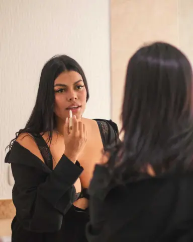 Young woman in a black lace robe applying lipstick in a bathroom mirror for a glamorous morning routine.