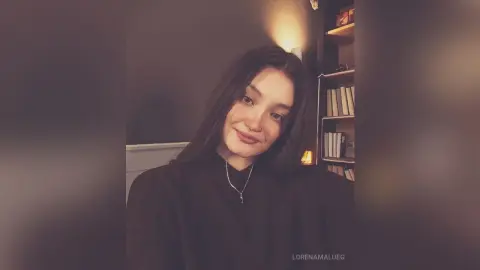 Smiling young woman in a black turtleneck sweater posing in a cozy, dimly lit room.
