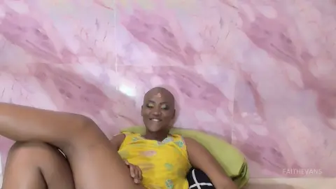Smiling woman in a yellow sleeveless top relaxing against a pink marble wall background.