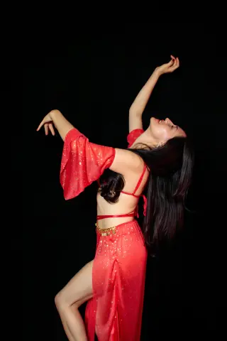 Joyful woman in a flowing red sparkly outfit dancing against a black background.