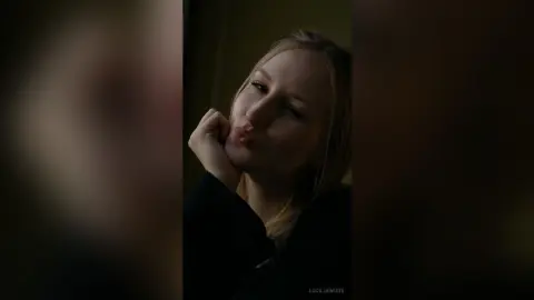 Blonde woman in a black outfit making a playful kissy face in moody, low-light indoor setting.