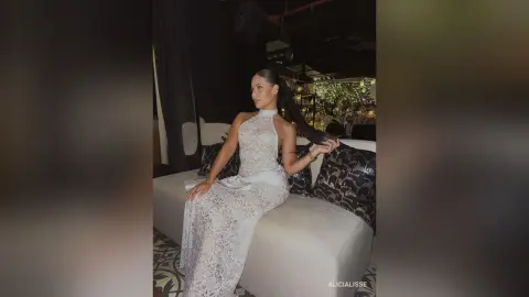 Elegant woman in a white lace halter gown sitting on a white sofa in a moody, dimly lit room.