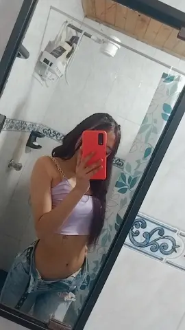 Young woman in a lilac crop top and denim jeans taking a mirror selfie in a bright bathroom.