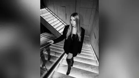 Elegant woman in a black blazer and boots walking down a modern marble staircase in a moody black and white setting.