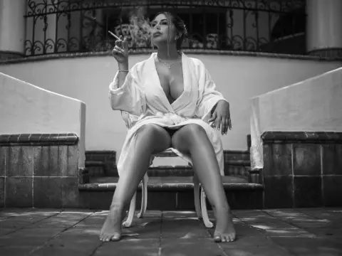 Moody black and white portrait of a woman in a white robe sitting on outdoor stairs smoking a cigarette.