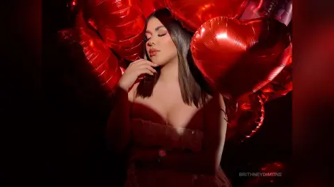 BrithneyDimons poses with long dark hair and cleavage, surrounded by red heart-shaped balloons.