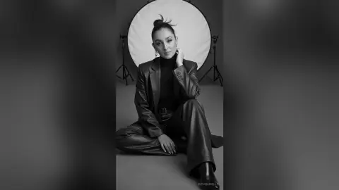 Elegant woman in a black leather suit sitting in a professional studio setting for a moody black and white portrait.